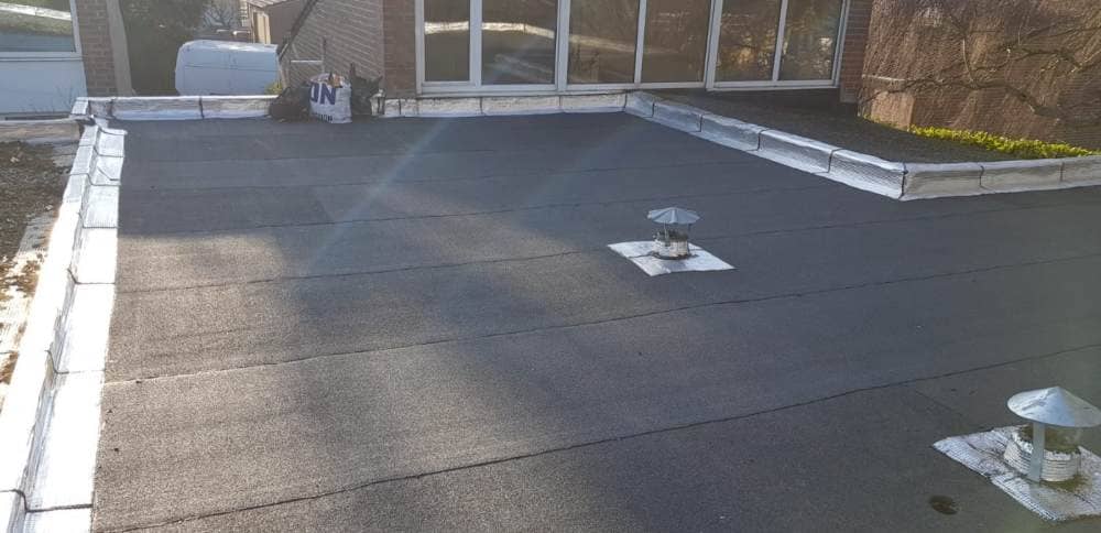 Toiture plate recouverte d'une étanchéité bitumeuse, avec chapeau de ventilation et relevés en zinc