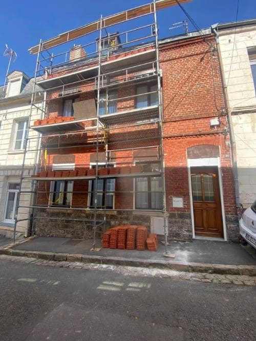 Façade de maison en brique sous échafaudage, tuiles neuves stockées sur les planchers pour la réfection de la couverture