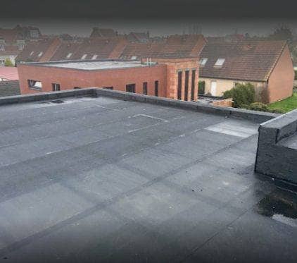 Toit plat terminé, recouvert d'une membrane EPDM noire avec ses relevés, devant une rangée de maisons en brique