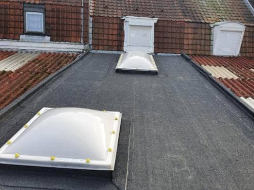 Toit plat en bitume entre deux toitures en tuiles, avec deux dômes de toit opalins