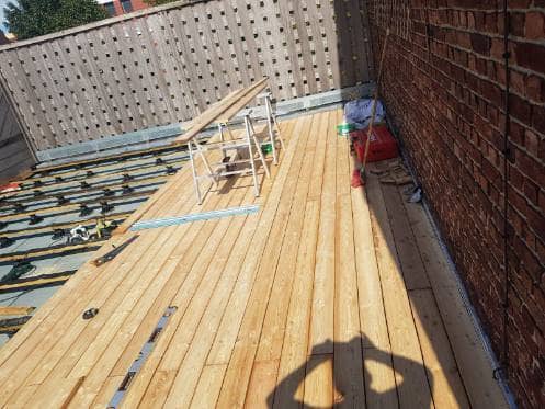 Pose des lames de bois d'une terrasse sur toit plat, lambourdes encore visibles sur la partie restante