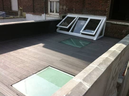 Toit-terrasse en lames composites avec dalles de verre praticables et châssis vitré, entre deux murs en brique