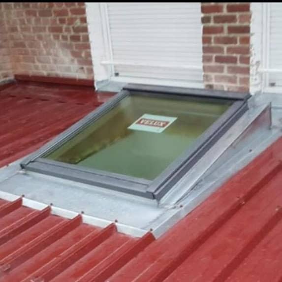 Fenêtre de toit Velux posée sur une couverture en bac acier rouge, avec son raccord en tôle