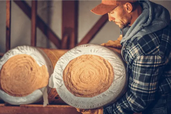 Un couvreur portant des rouleaux de laine de verre